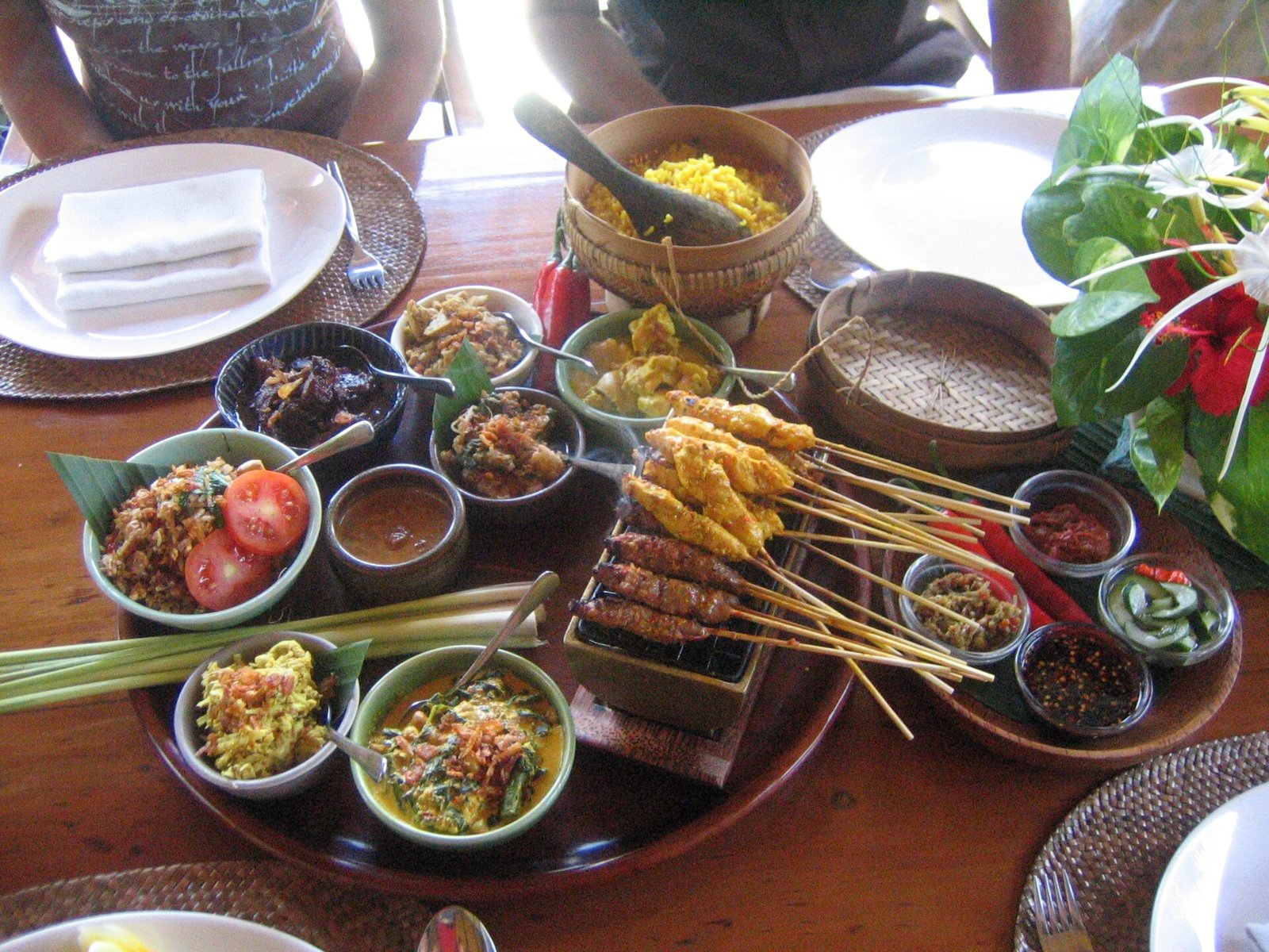 Aneka hidangan Bali dalam satu meja: sate, sambal, dan lauk-pauk dalam mangkuk kecil, disajikan bersama di atas nampan kayu.