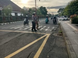Personel Satuan Lantas Polsek Gianyar membantu seorang lansia menyeberang jalan menuju Alun-Alun Gianyar.