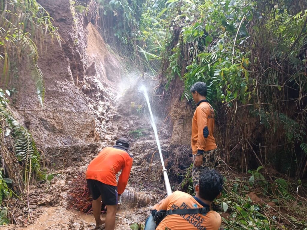 Petugas menyemprotkan air ke tanah longsor yang menimbun saluran irigasi.