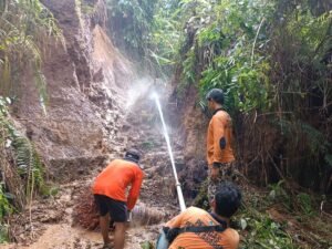Petugas menyemprotkan air ke tanah longsor yang menimbun saluran irigasi.