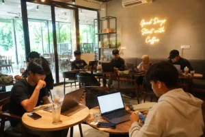 Anak muda bekerja dengan laptop di coffee shop Bali sebagai ilustrasi mencari penghasilan tambahan di Bali melalui pekerjaan online dan freelance.