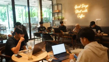 Anak muda bekerja dengan laptop di coffee shop Bali sebagai ilustrasi mencari penghasilan tambahan di Bali melalui pekerjaan online dan freelance.
