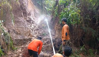 Petugas menyemprotkan air ke tanah longsor yang menimbun saluran irigasi.